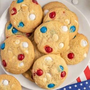 A plate of cookies with red, white, and blue candy pieces, arranged on a white surface next to part of a flag-themed cloth.
