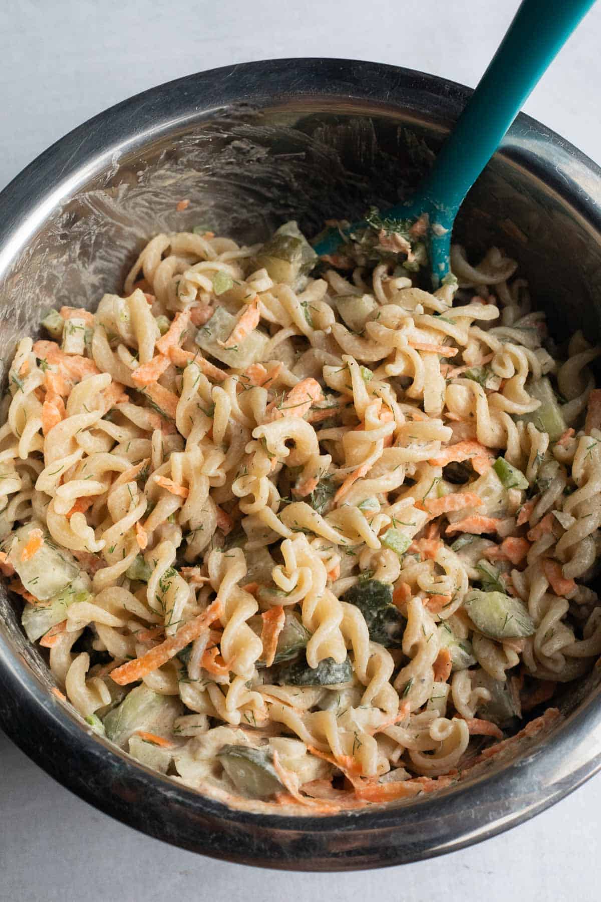 A bowl of creamy Pickle Pasta Salad featuring spiral noodles, shredded carrots, and chopped vegetables.