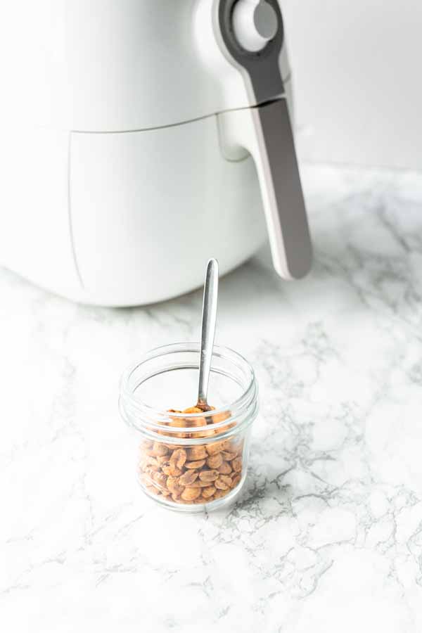 Roasted Air Fryer peanuts in a glass jar with a spoon. Easy to make yourself in no time.