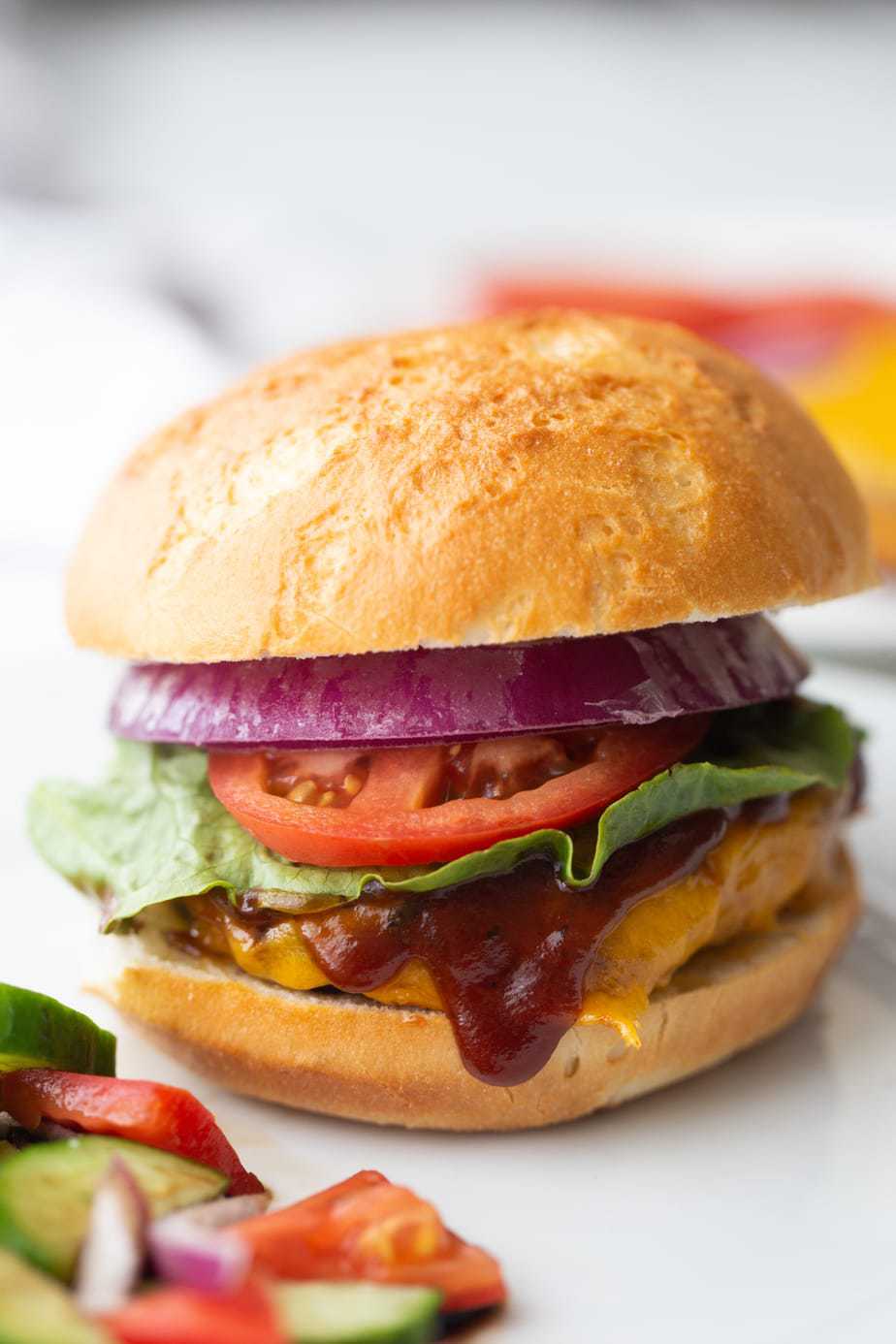A close up of a BBQ Chicken Burger with lettuce, onion, tomatoes and an extra drizzle of BBQ sauce 