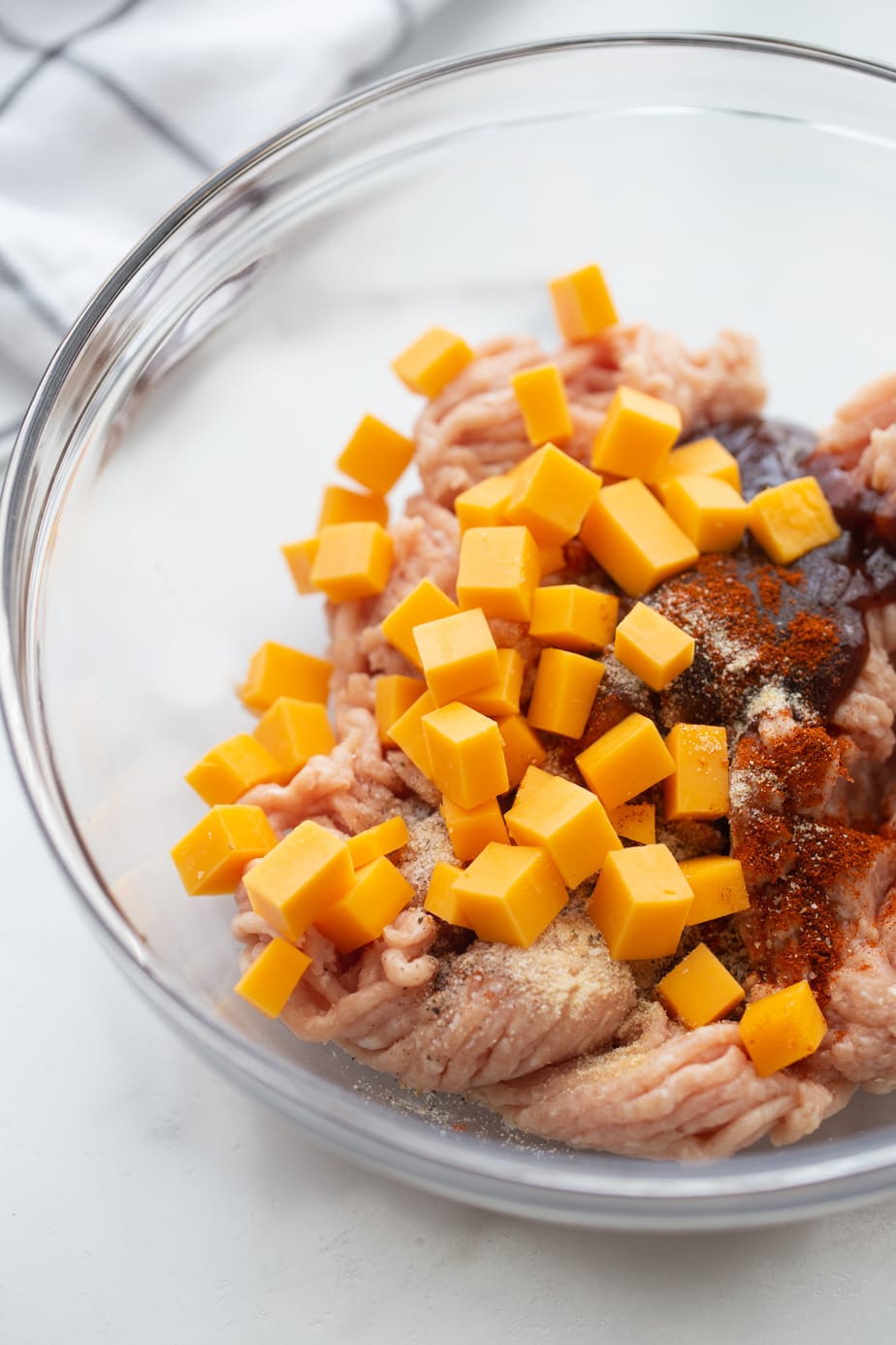 A bowl of ground chicken, cheese cubes and seasonings