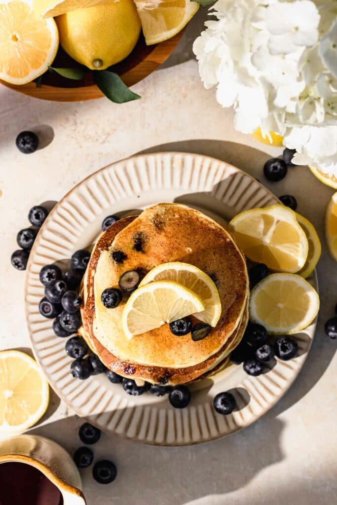 Stack of blueberry lemon pancakes on plate with lemon slices and flowers