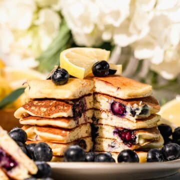 stack of blueberry lemon pancakes with peak inside. Topped with lemon slices and fresh blueberries