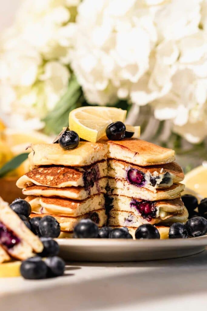 stack of blueberry lemon pancakes with peak inside. Topped with lemon slices and fresh blueberries