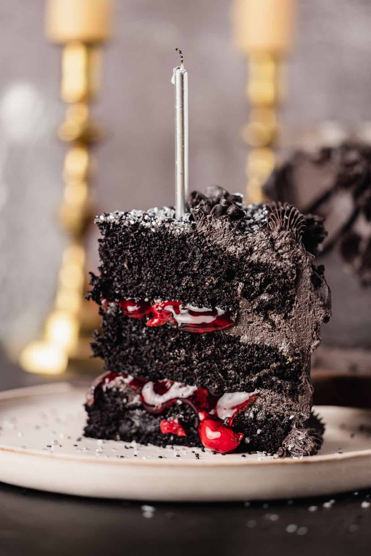 slice of black velvet cake with candle, black frosting, and a bright red cherry filling