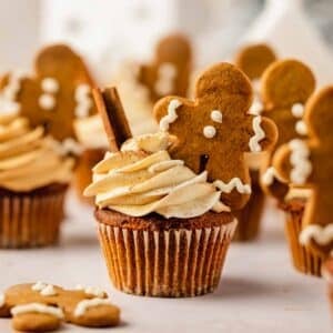 gingerbread cupcakes with gingerbread frosting and mini gingerbread men with evergreen tree in the back