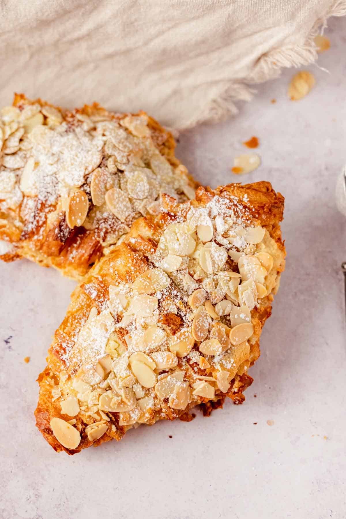 almond croissant on counter topped with sliced almonds and dusted with powdered sugar