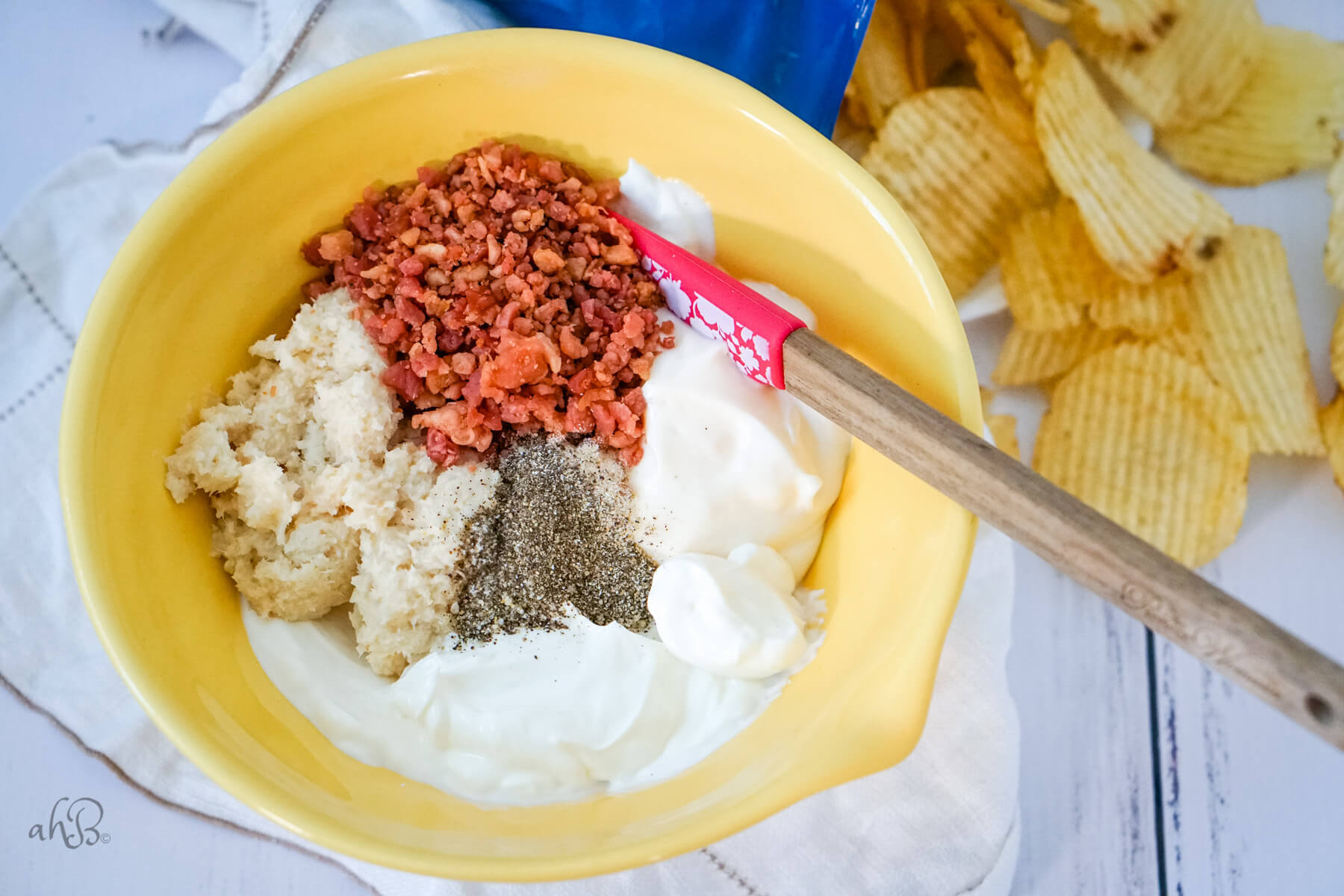 The ingredients are all added to a yellow bowl and stirred with a spatula.