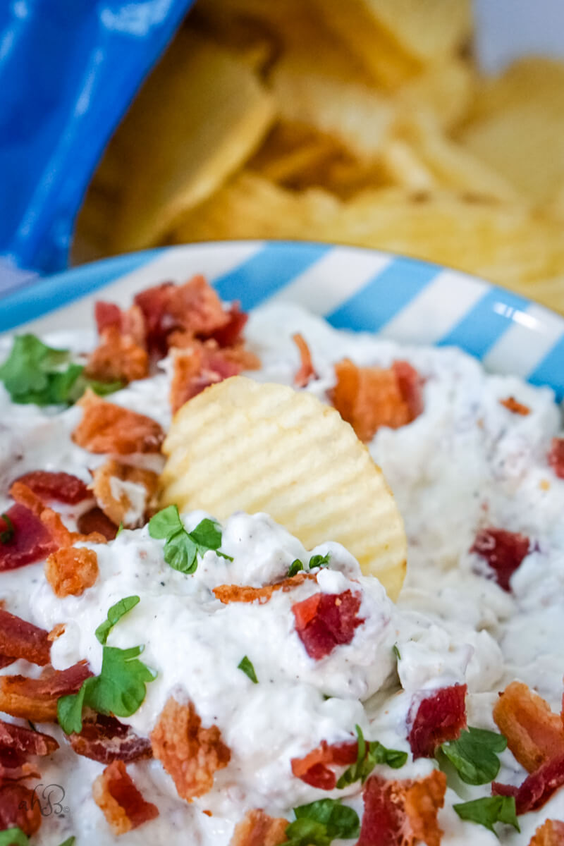 A chip sits in the bowl of bacon horseradish dip.