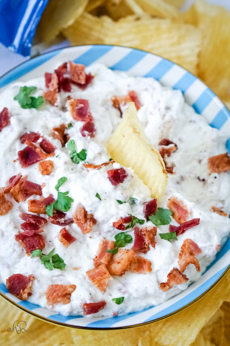 A potato chip sits in the bowl of bacon horseradish dip.