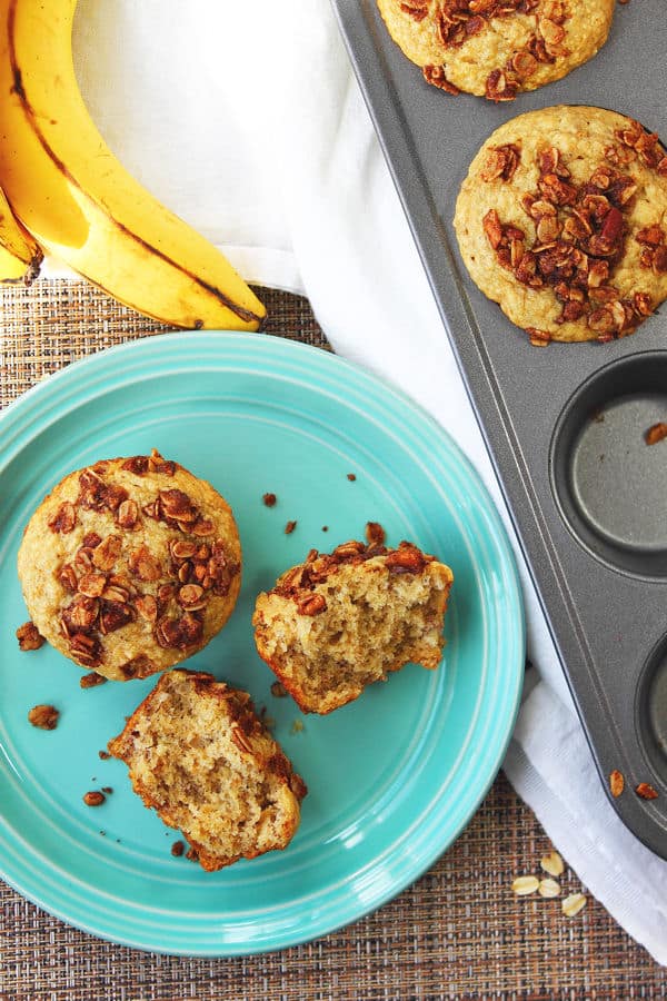 a couple of oatmeal banana muffins on a teal green plate with one cut open alongside the muffin tin with more inside there