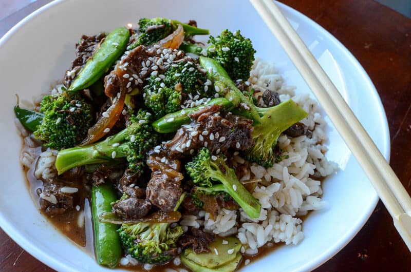 beef and broccoli over rice in a white bowl with chopsticks