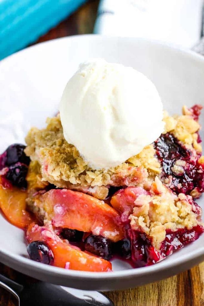 A bowl of blueberry peach crisp with a scoop of vanilla ice cream