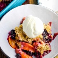 A bowl of blueberry peach crisp with a scoop of vanilla ice cream