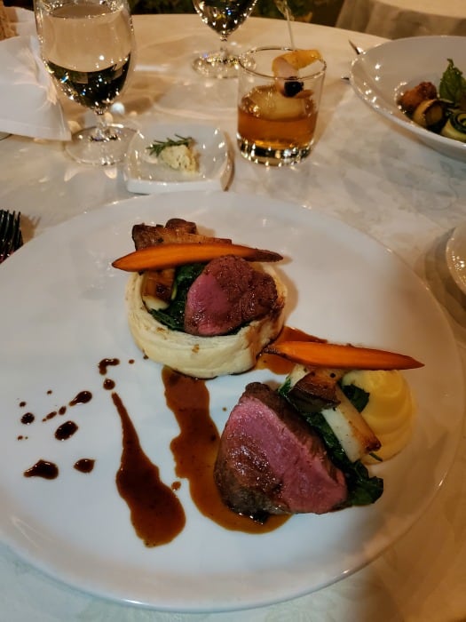 filet mignon with potatoes on a white plate next to a cocktail and glass of water and Erna's Elderberry 