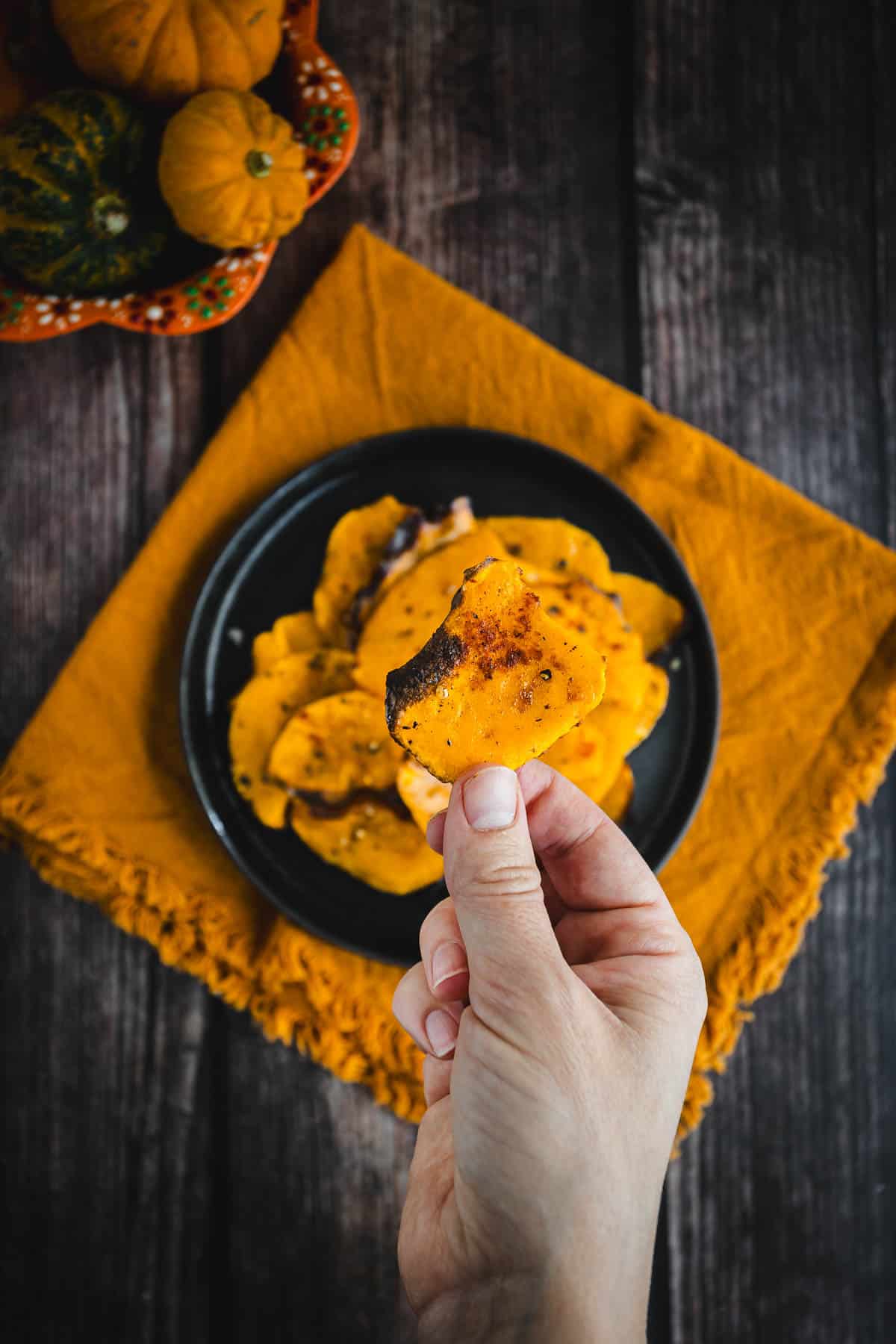 A hand holding a piece of butternut squash chips on a plate.