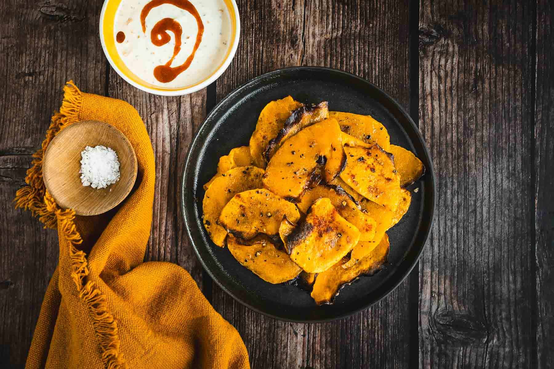 Roasted butternut squash chips on a plate next to a bowl of sauce.
