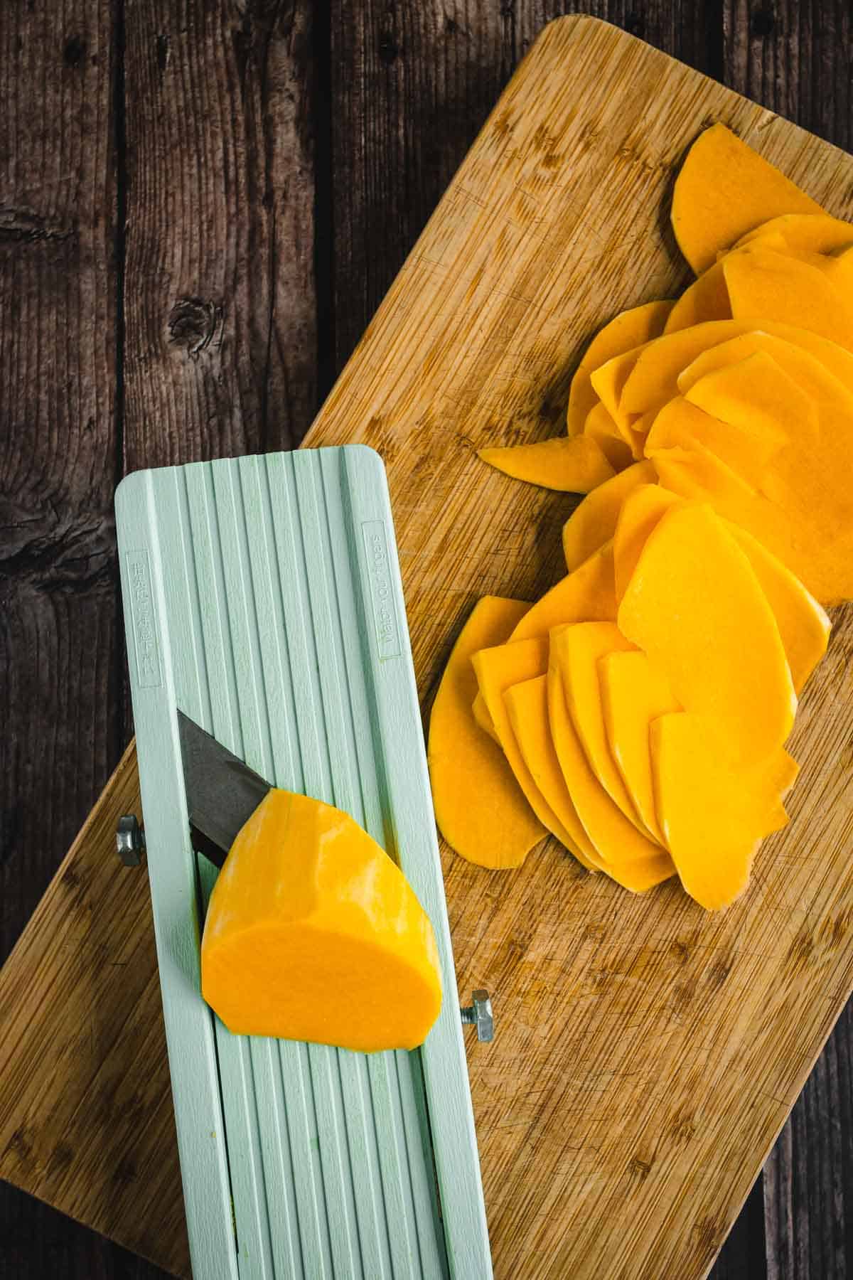 butternut squash slices on a cutting board with a knife.