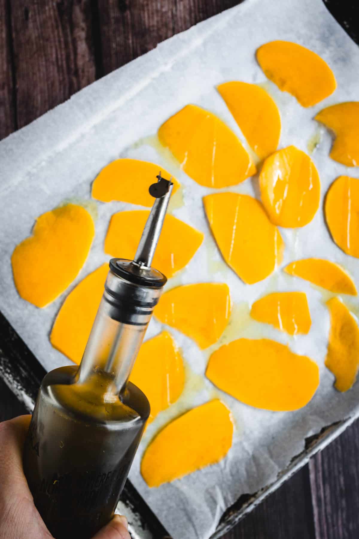 A person is pouring oil on a baking sheet.