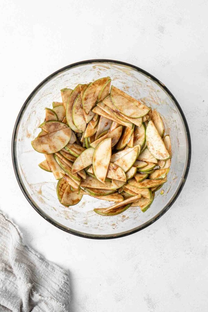 Mixing the apples with spices and caramel sauce in a glass bowl.