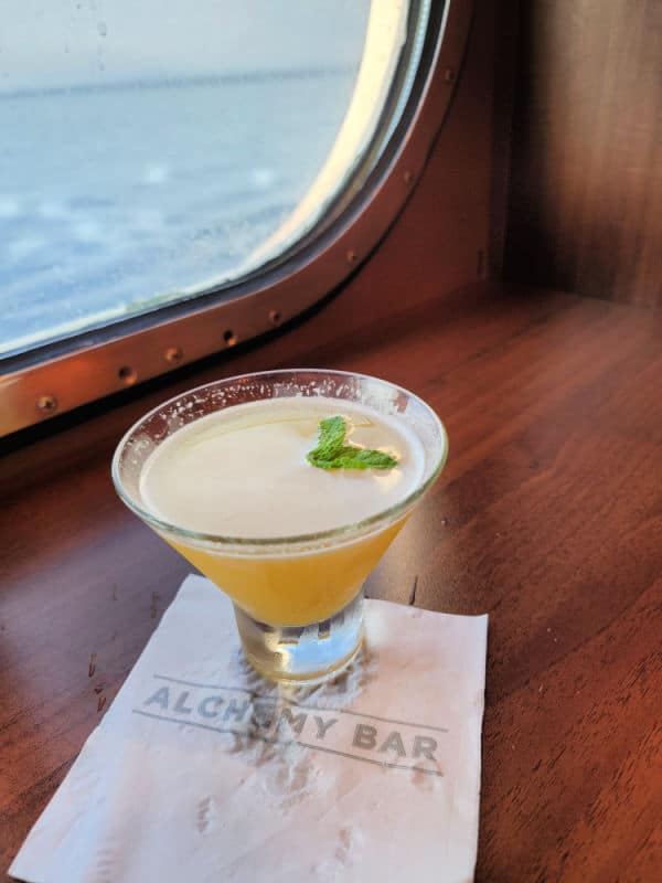 Carnival Alchemy bar napkin under a Spicy Chipotle Martini on a wooden shelf by the window