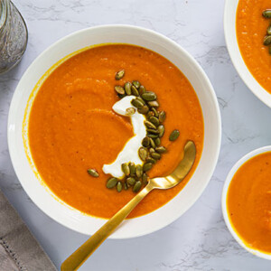 Overhead view of Carrot Orange Soup topped with pumpkin seeds in white bowls on a white marble table