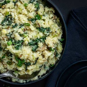 Overhead view of Cauliflower Colcannon in a dark blue bowl on a black background