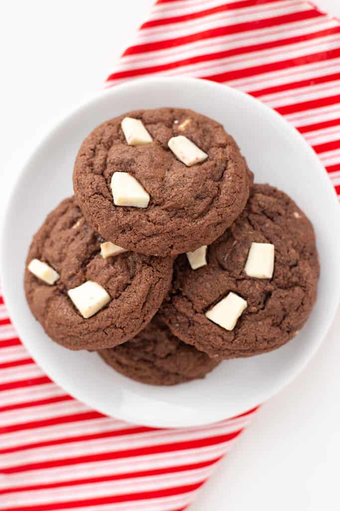 overhead photo of chocolate cookies on a white plate with a striped fabric under it