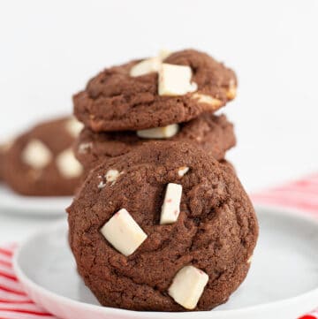 stack of cookies with another cookie leaned on the stack on a white plate with a candy cane striped linen
