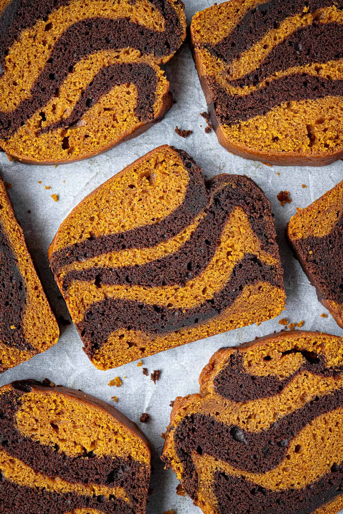 Slices of pumpkin chocolate marble bread on a sheet of baking parchment.