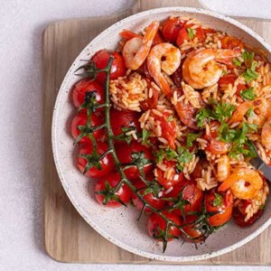 Chorizo and Shrimp Paella in a white skillet on top of a wooden cutting board