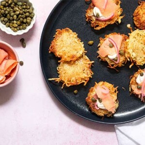 Classic Latkes on a black plate topped with cream cheese and lox