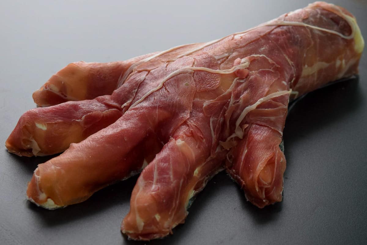 Close up view of cream cheese dip shaped hand wrapped in prosciutto