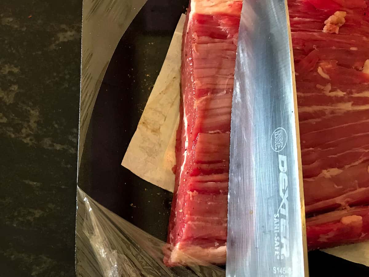 Knife positioned against the grain of flank steak.