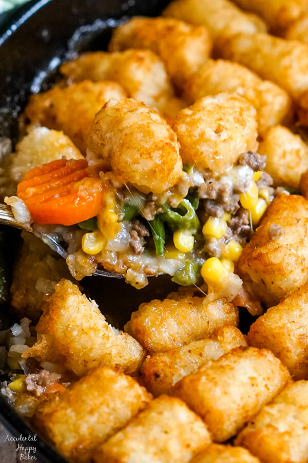 A spoonful of Shepherd's Pie with Tater Tots is scooped out of the skillet. 