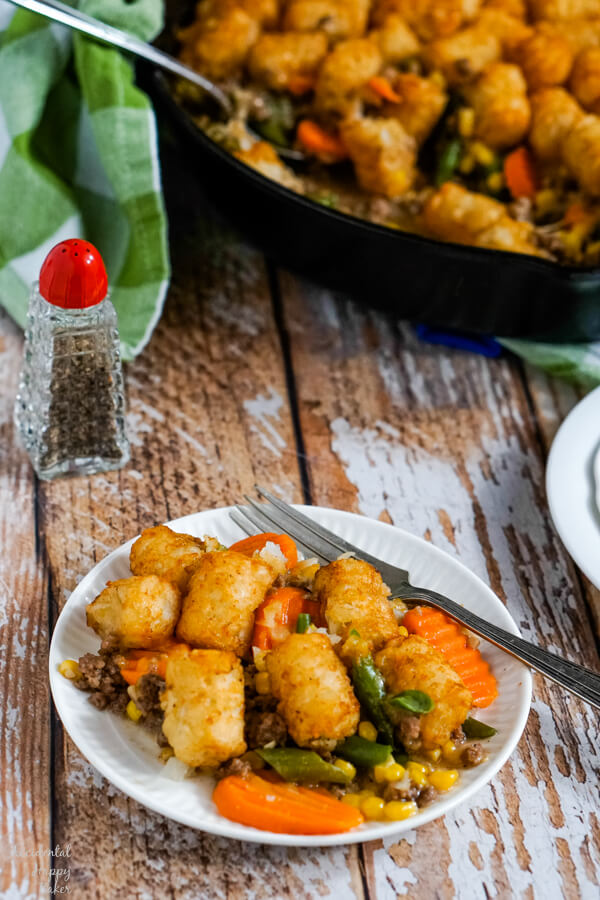 A plate of Shepherd's Pie with Tater Tots sits next to a cast iron skillet. 