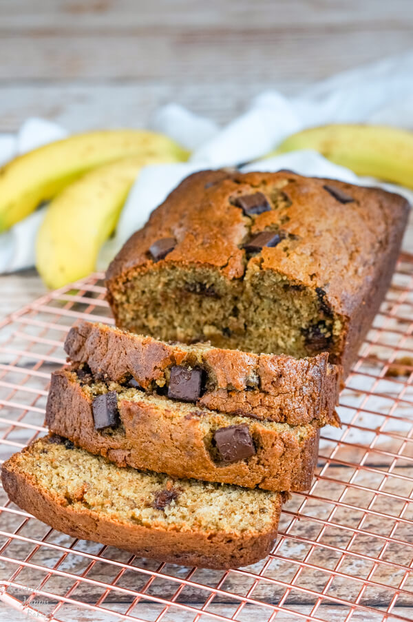 A loaf of chocolate chunk banana bread sliced and sitting on a copper cooling rack.