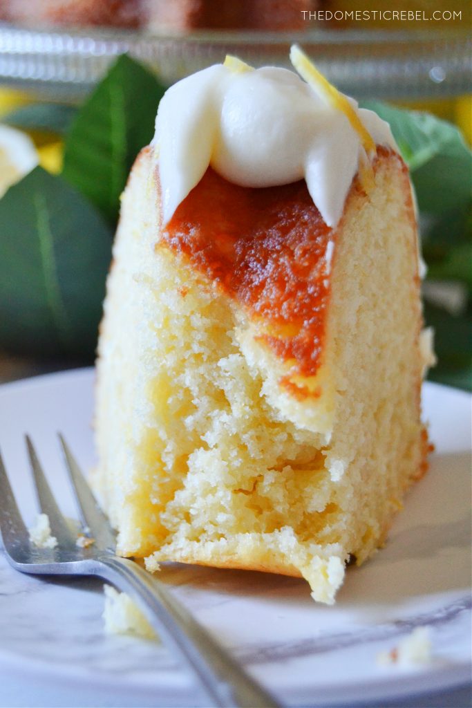 Closeup of lemon bundt cake on marble plate with a silver fork and a bite missing