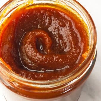 Easy Crockpot Pumpkin Butter in Glass Jar on White Marble Background.