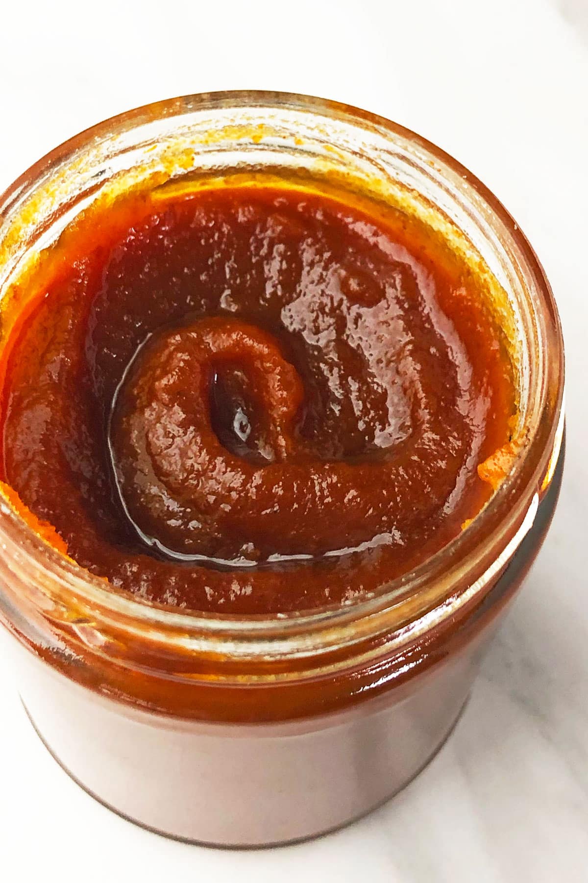 Easy Crockpot Pumpkin Butter in Glass Jar on White Marble Background.