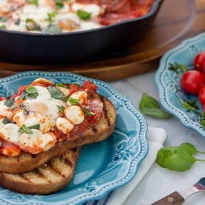 Gluten Free Eggs alla Pizzaiola on a blue plate with fresh tomatoes in the background