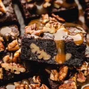 Close-up of chocolate turtle brownies with visible pecans, topped with a drizzle of caramel sauce and extra pecan pieces.
