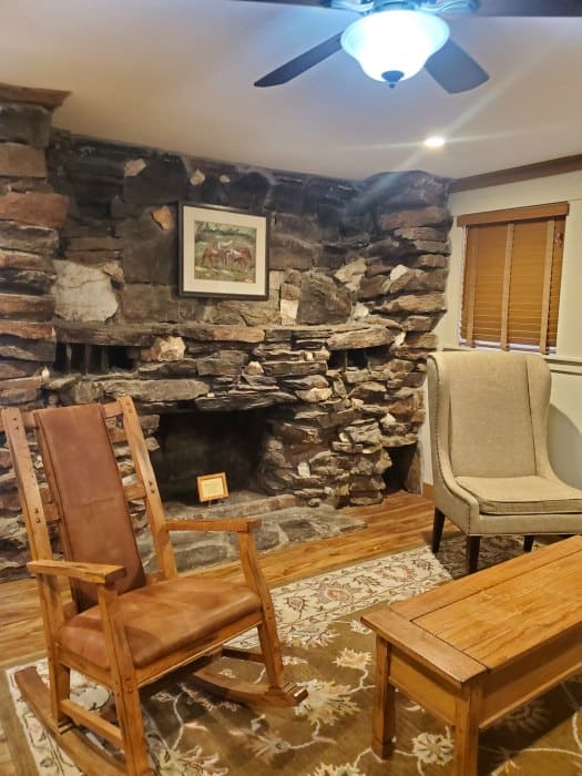 rock fireplace behind a rocking chair and cloth chair next to a long table 