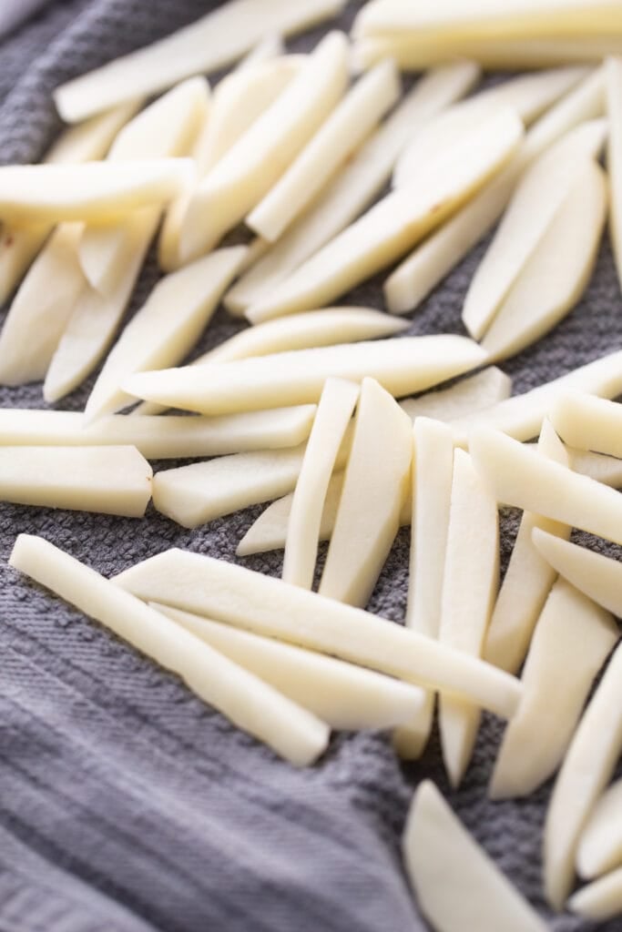 Thin cut raw potatoes drying on a dark gray kitchen towel, ready for the air fryer or oven.