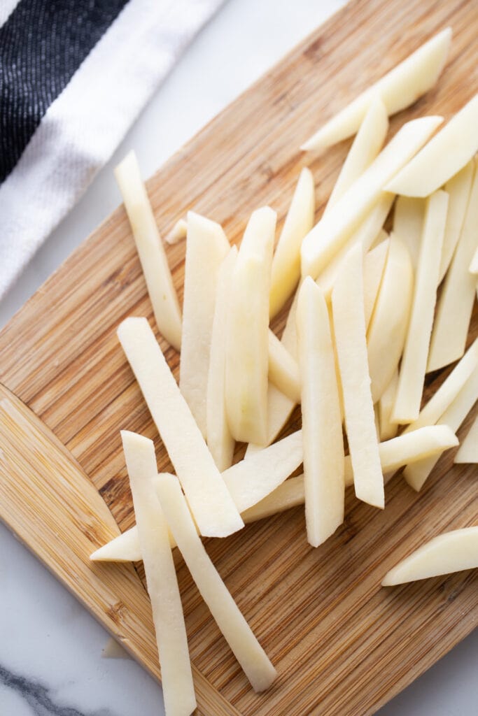 Thin sliced raw potatoes on a wooden cutting board, ready for the oven or air fryer.