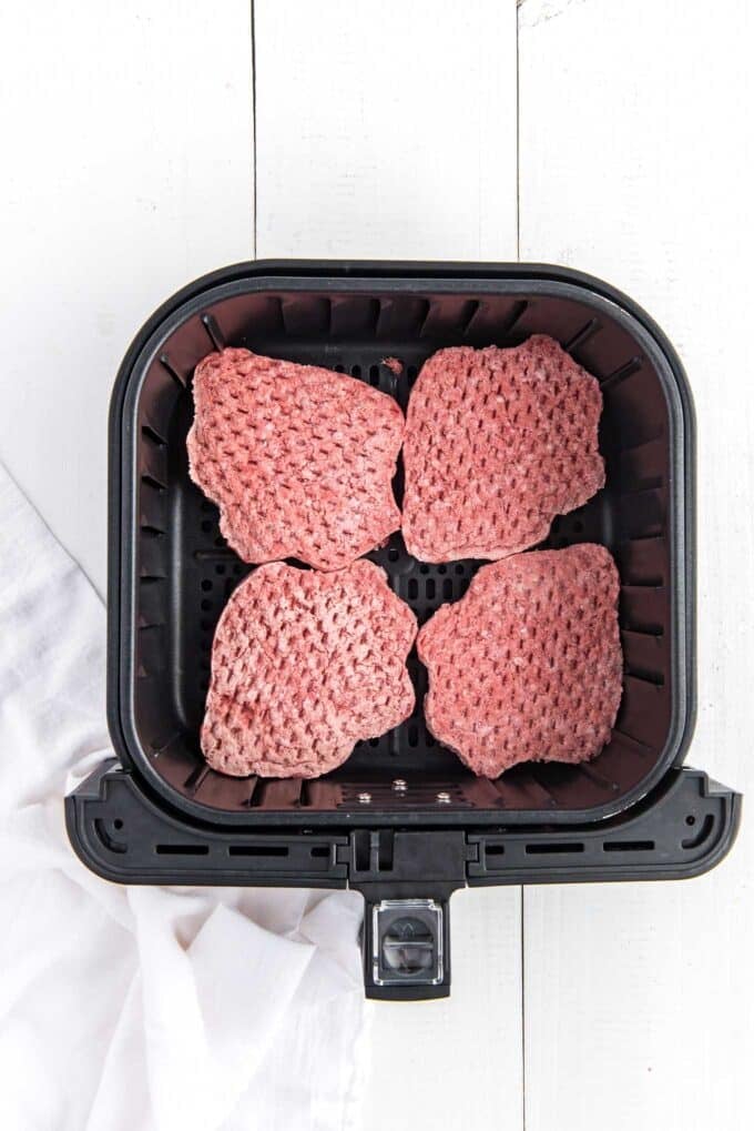 Frozen burger patties lined up in the basket of an air fryer.