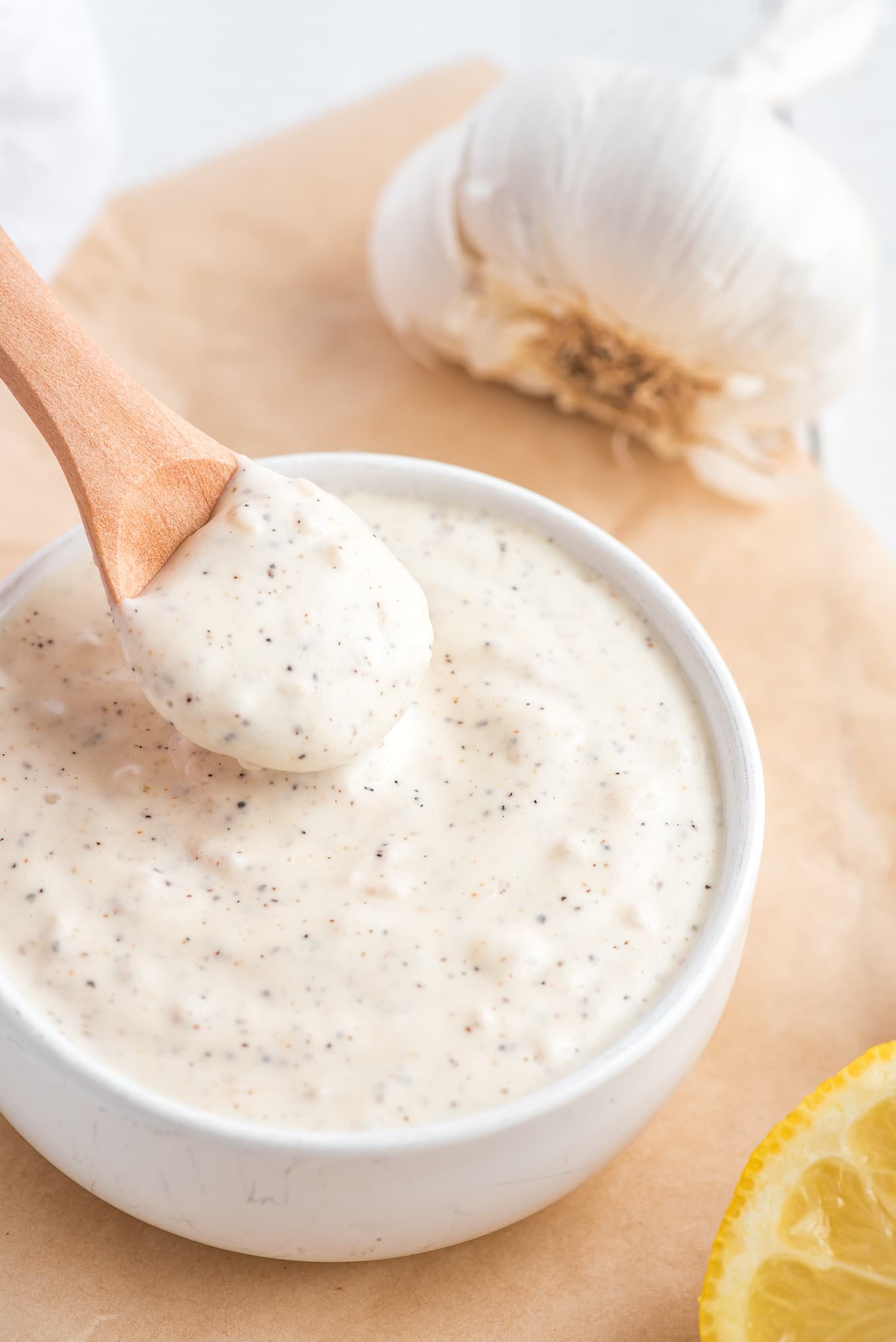 A bowl of garlic aioli mayo on the table with a spoonful up above it.