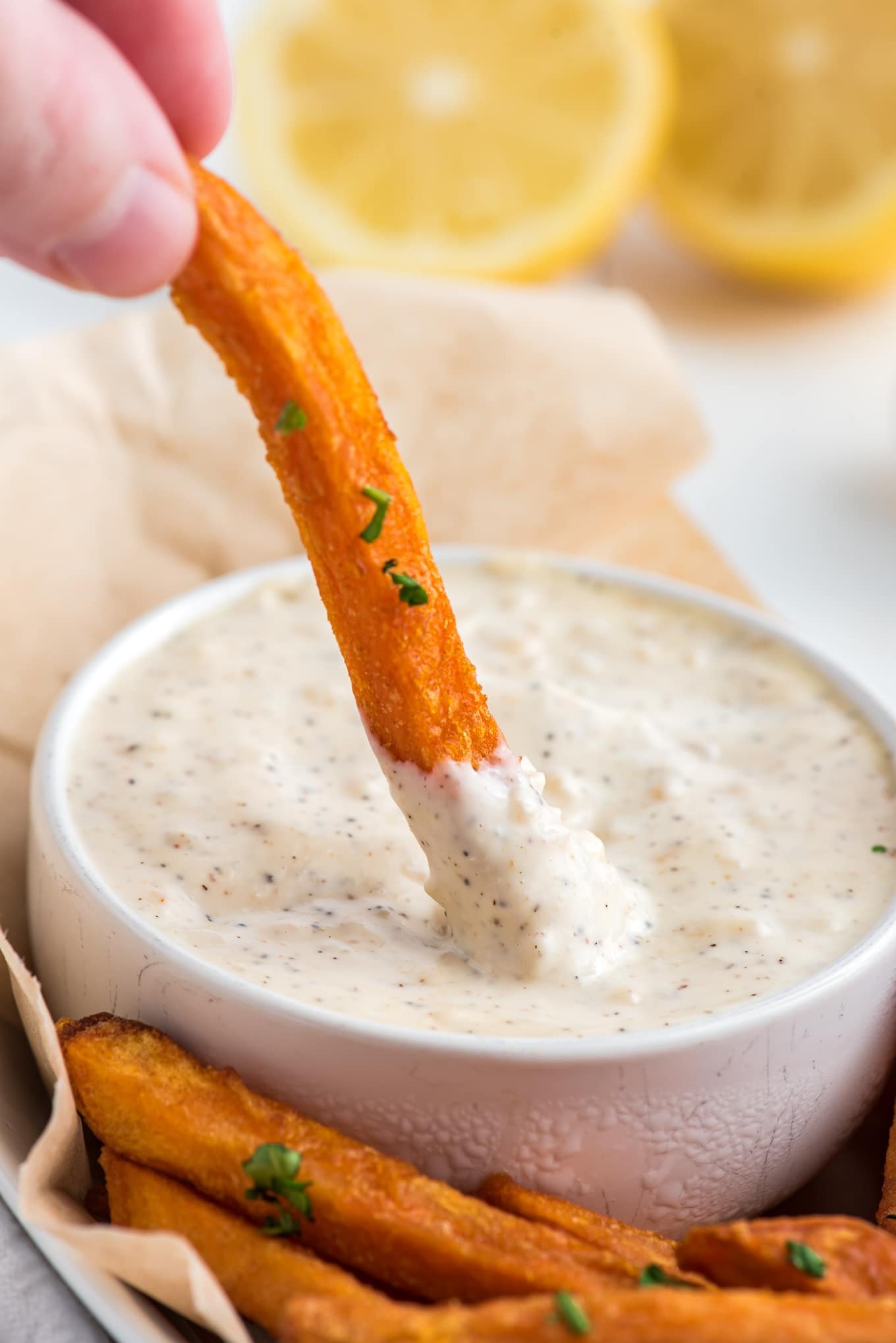 A hand dipping a fry into a bowl of garlic aioli.