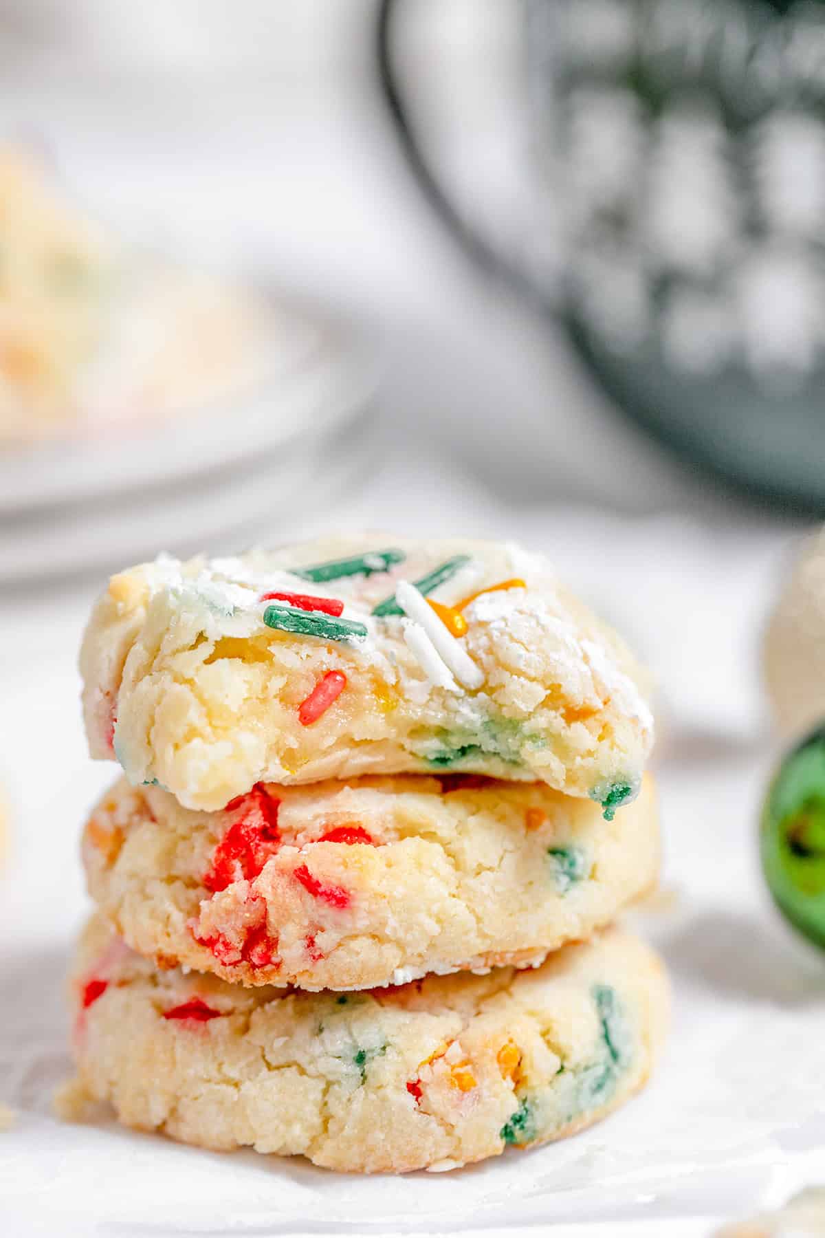 A stack of three gooey butter cookies, adorned with colorful sprinkles, rests on a white surface against a softly blurred background.