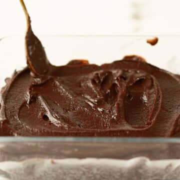 Ganache frosting being spread on top of brownies.